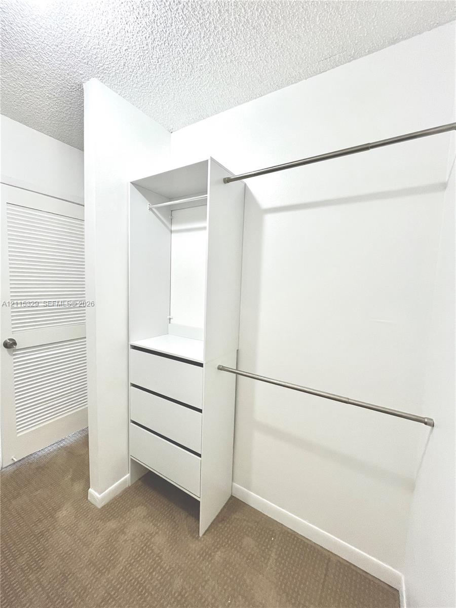 Walk-in closet featuring built-in white cabinetry, three integrated storage drawers, dual-level metal garment rods, and louvered door entry
