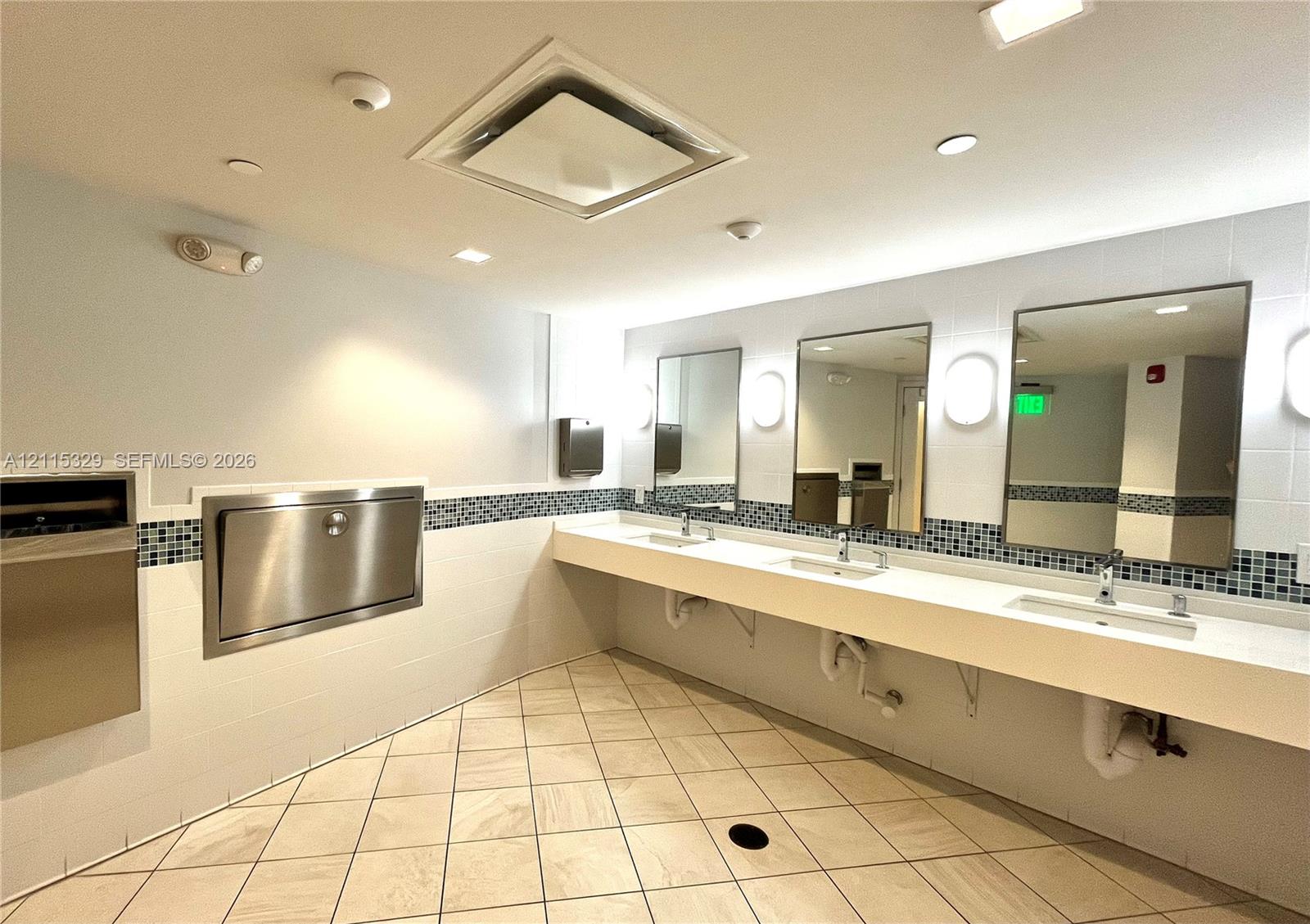 Triple-basin vanity featuring an extended solid-surface countertop, three rectangular undermount sinks with polished chrome faucets, wall-mounted rectangular mirrors, and tiled flooring