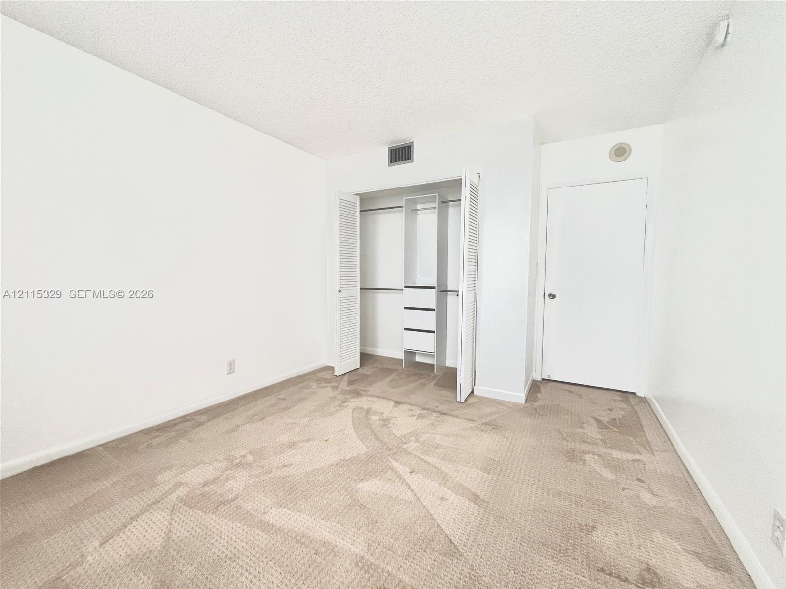 Neutral-toned carpeting, closet with louvered double doors, and built-in closet shelving unit featuring drawers
