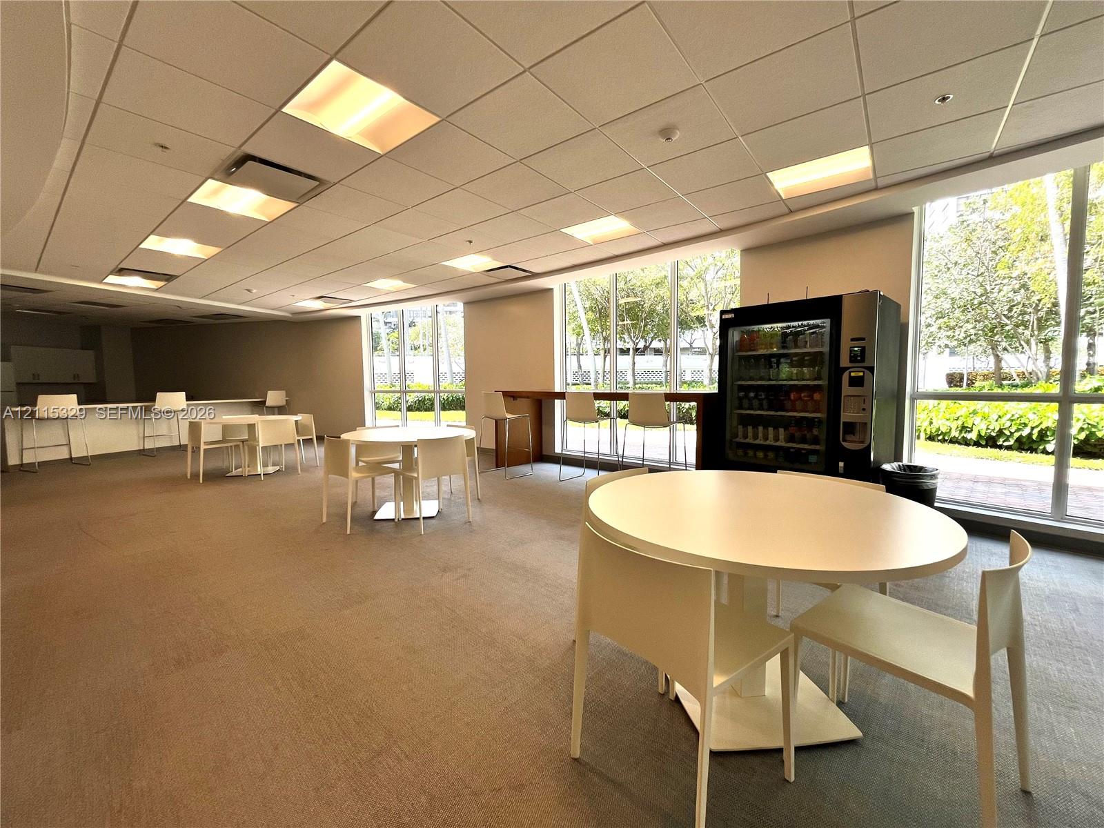 Open-concept space featuring floor-to-ceiling windows, drop-tile ceiling with recessed lighting, and neutral carpeting