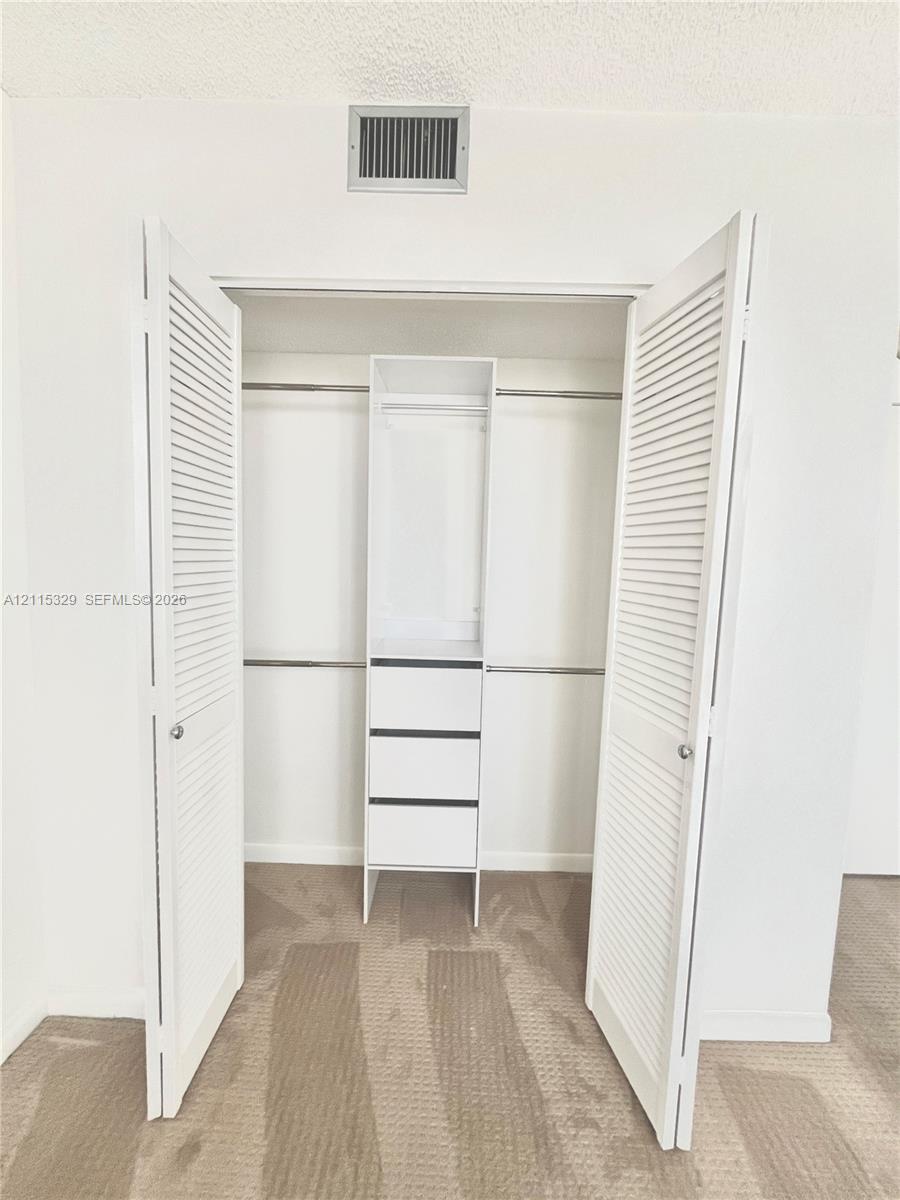 Closet featuring white louvered doors, built-in shelving with three integrated drawers, and dual hanging rods