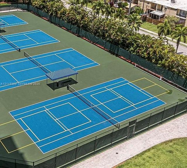 Multiple tennis courts featuring blue playing surfaces, perimeter fencing, and shaded bench seating