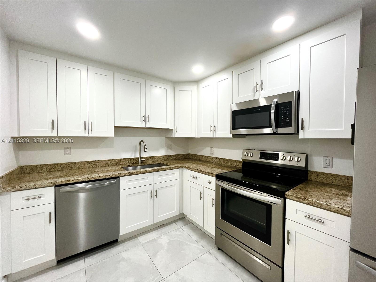 Kitchen featuring white shaker-style cabinetry, stone countertops, stainless steel appliances, and large-format tile flooring