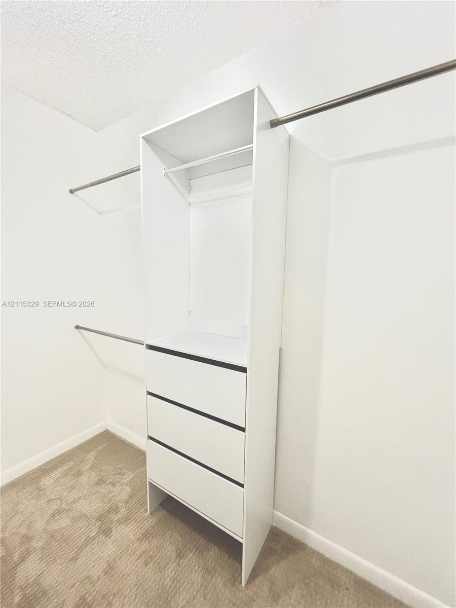 Walk-in closet featuring white built-in cabinetry, three drawers, an open shelving compartment, and metal clothing rods