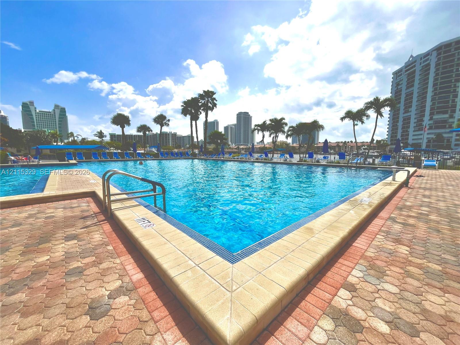 Swimming pool with tiled coping and metal railings, surrounded by a geometric paver deck and mature palm trees