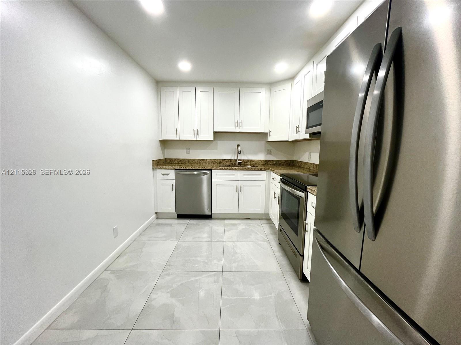 Kitchen featuring white cabinetry, stone-finish countertops, stainless steel appliances, and large-format tile flooring