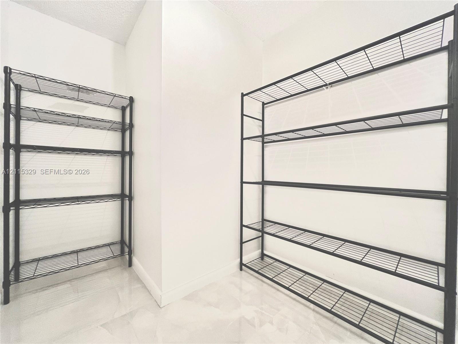 Storage area featuring neutral tile flooring, white walls, and black metal wire shelving units