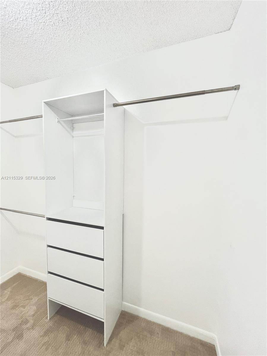 Walk-in closet featuring white built-in cabinetry, three storage drawers, and dual-level metal hanging rods