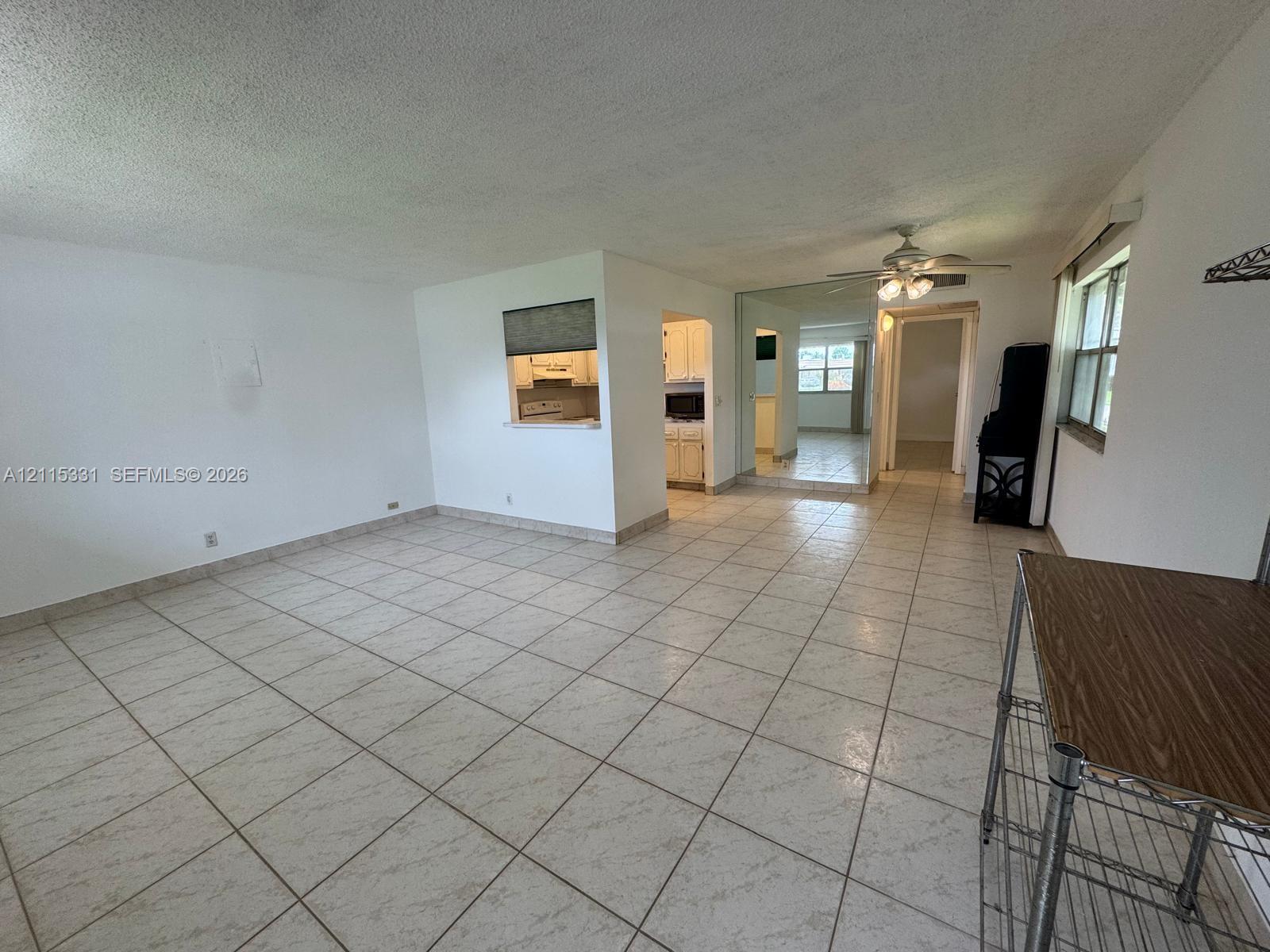 Open-concept interior featuring light-colored ceramic tile flooring, a pass-through window to the kitchen, mirrored wall accents, and a ceiling fan with integrated lighting Open-concept interior featuring light-colored ceramic tile flooring, a pass-through window to the kitchen, mirrored wall accents, and a ceiling fan with integrated lighting