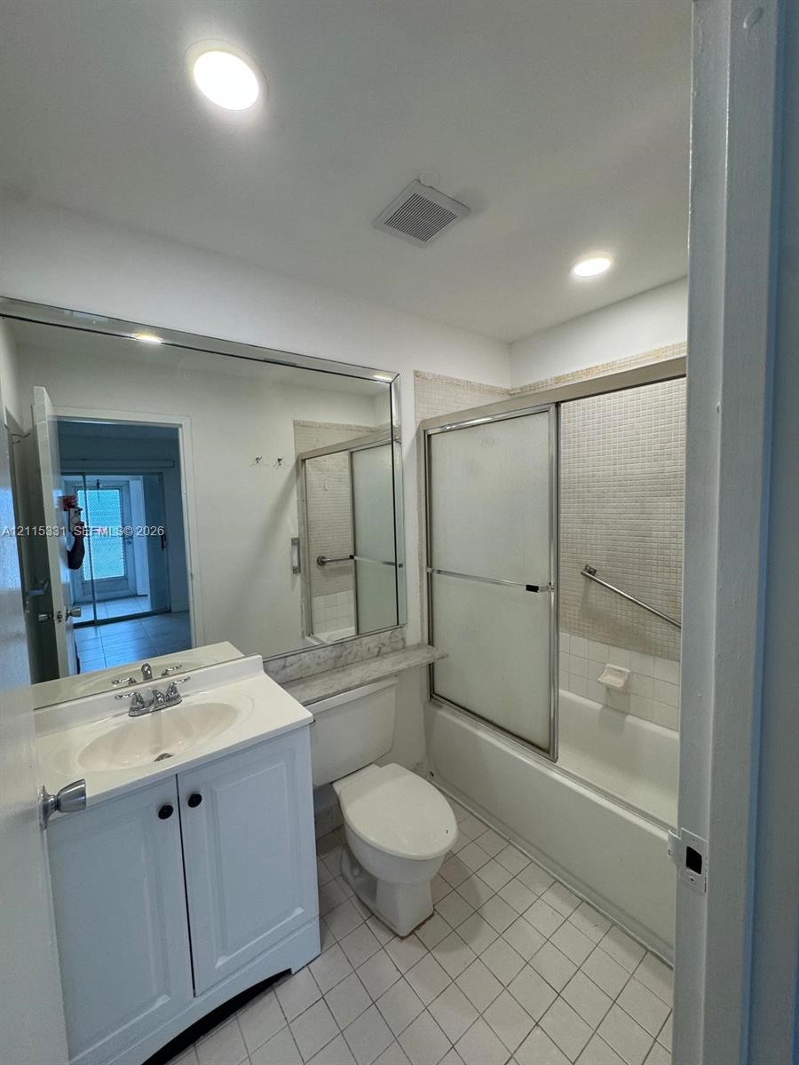 Bathroom featuring a vanity with an integrated sink and stone-finish countertop, full-width wall mirror, tub-shower combination with sliding glass doors, mosaic-tile shower surround, and square-tile flooring