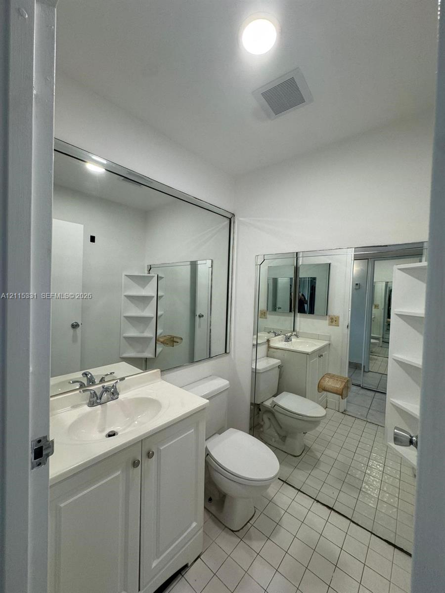 Bathroom featuring a white vanity cabinet with a integrated sink, large wall-mounted mirrors, tile flooring, and built-in shelving
