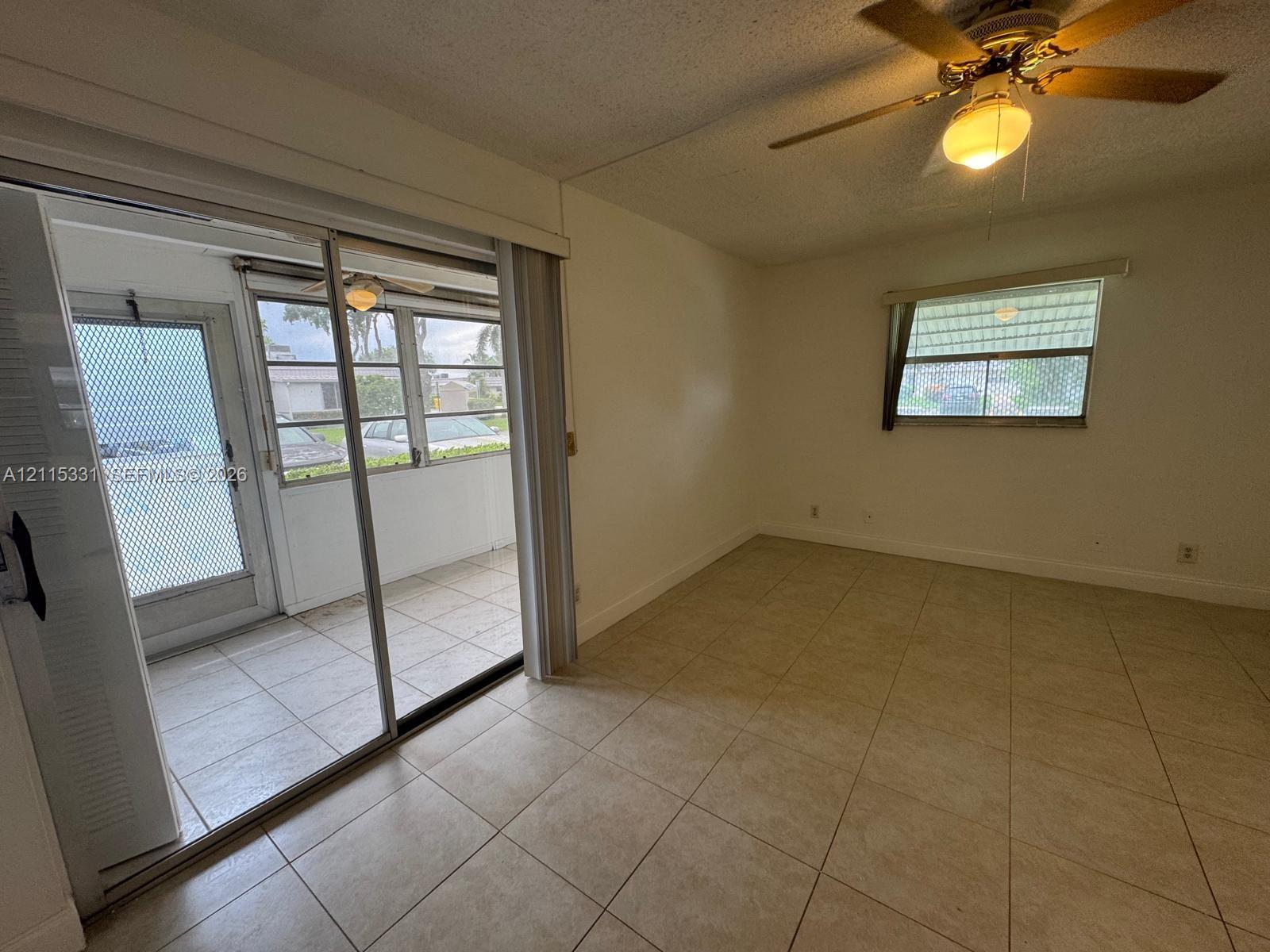 Ceramic tile flooring, sliding glass sunroom doors, ceiling-mounted light fixture with fan, and screened-in porch with tiled flooring