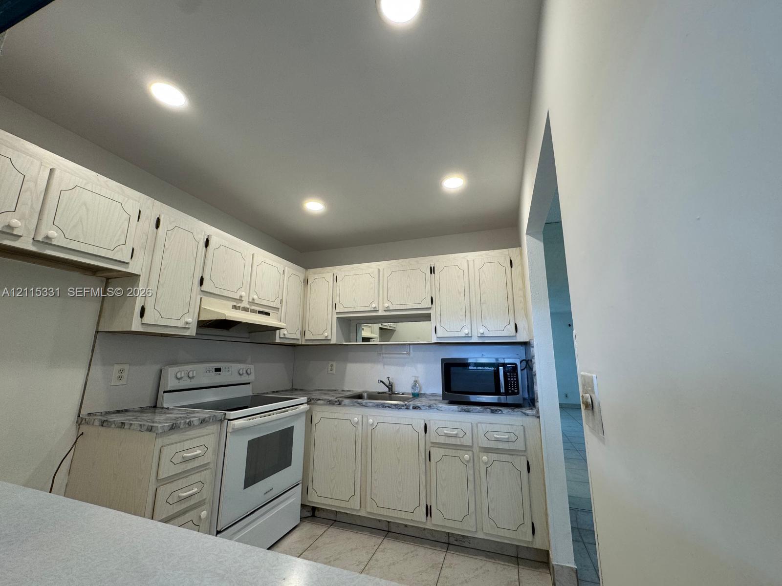 Kitchen featuring cabinetry with routed detailing, laminate countertops, recessed ceiling lighting, and tile flooring Kitchen featuring cabinetry with routed detailing, laminate countertops, recessed ceiling lighting, and tile flooring