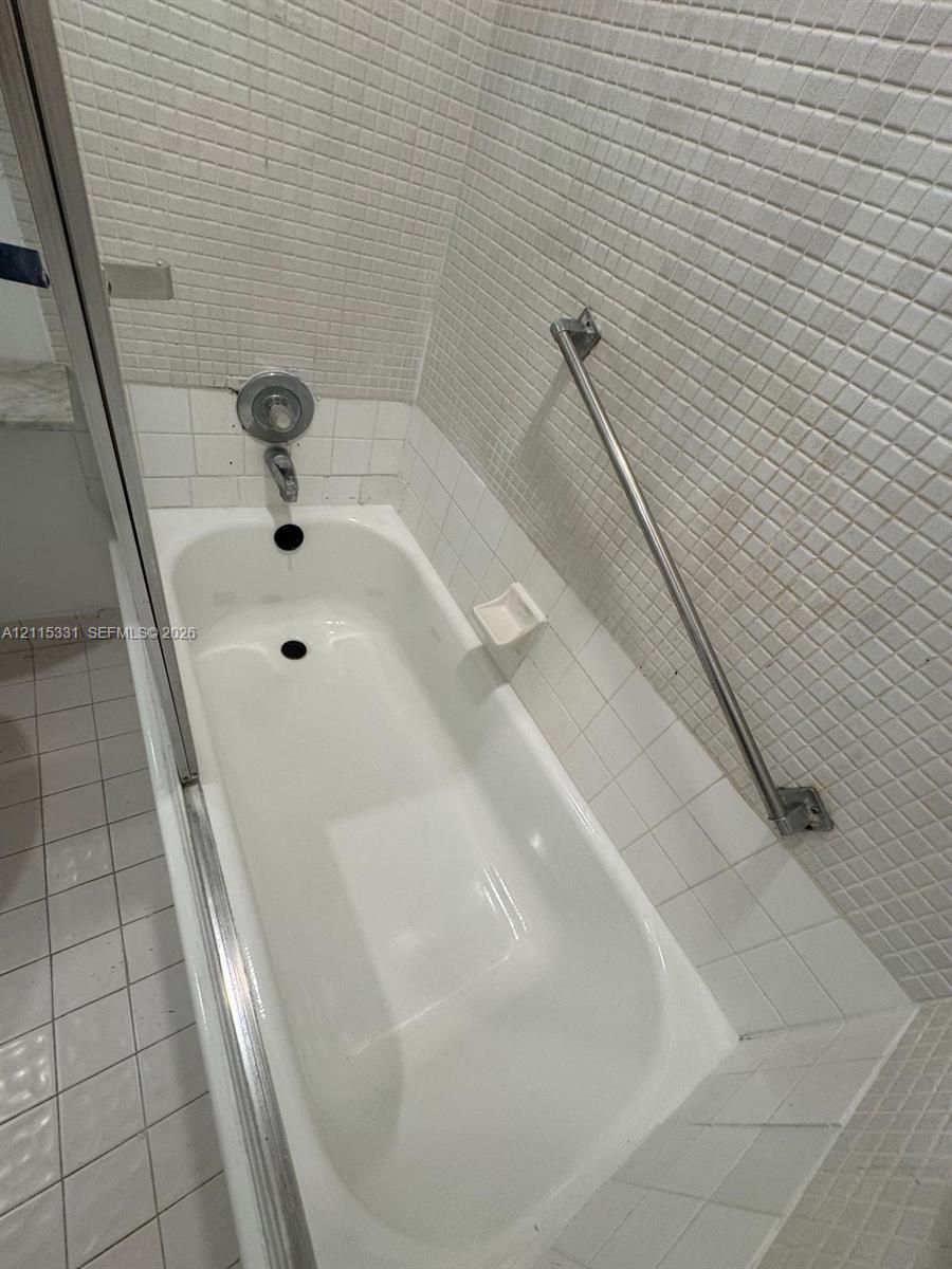 New Bathtub featuring tiled surround, stainless steel hardware, and metal grab bar