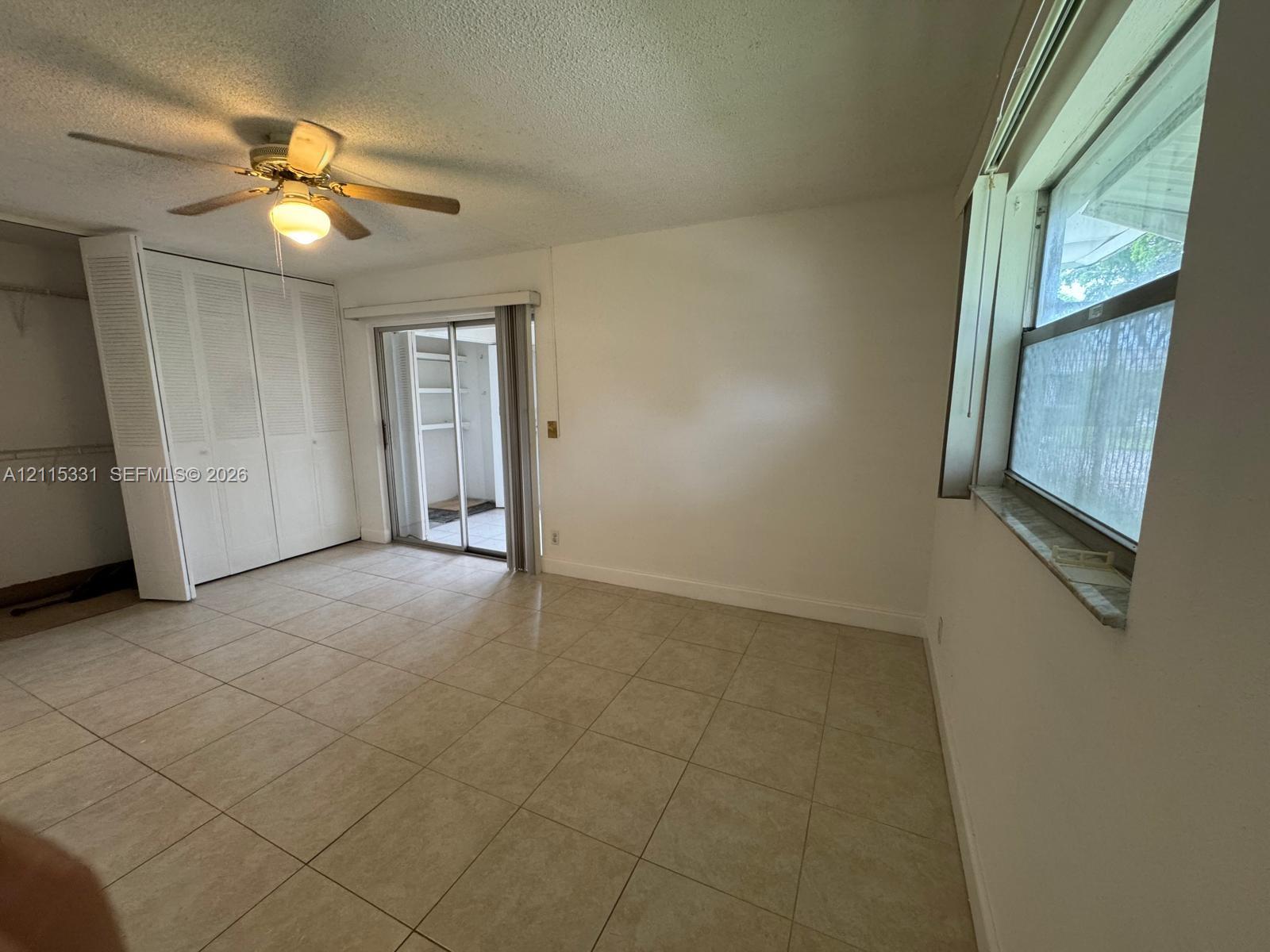 Interior space featuring neutral floor tiling, louvered-door closets, a ceiling fan with integrated lighting, and a sliding glass door providing access to an exterior enclosure