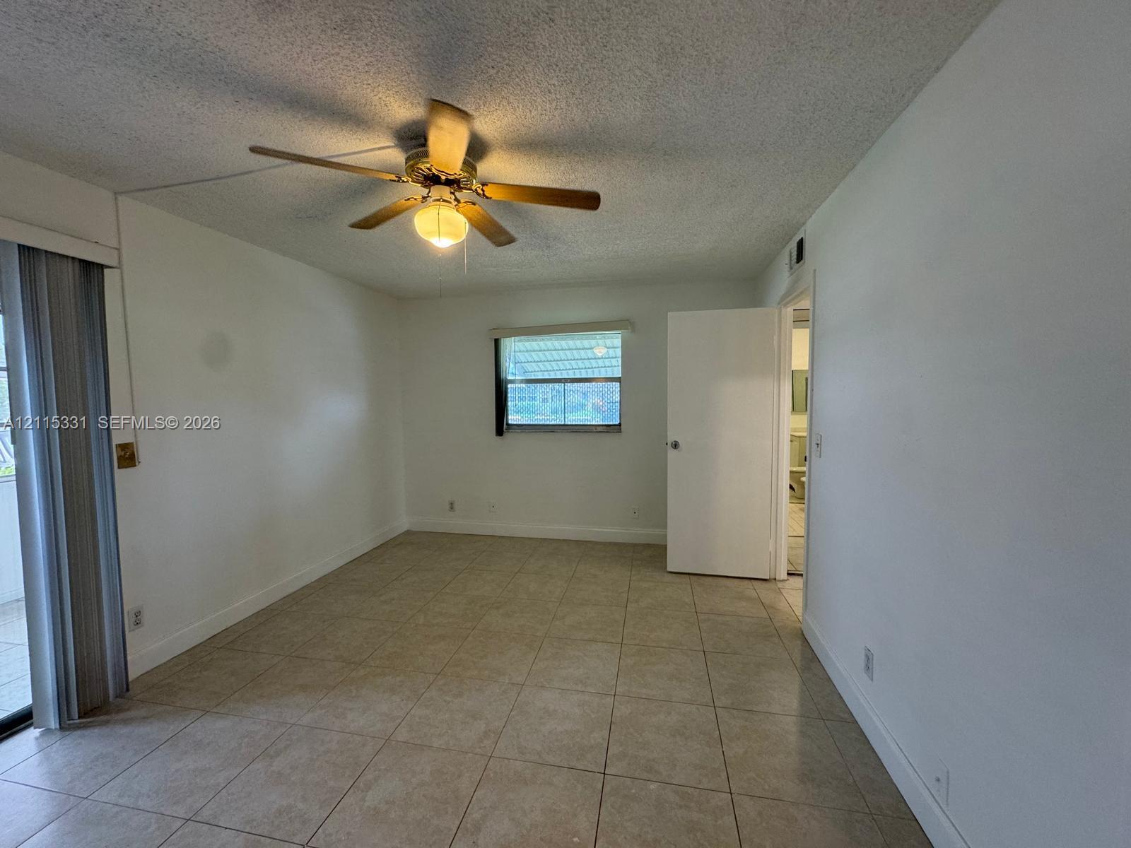 Tile flooring throughout, neutral interior paint, integrated ceiling fan with light fixture, sliding glass door, and window with natural light