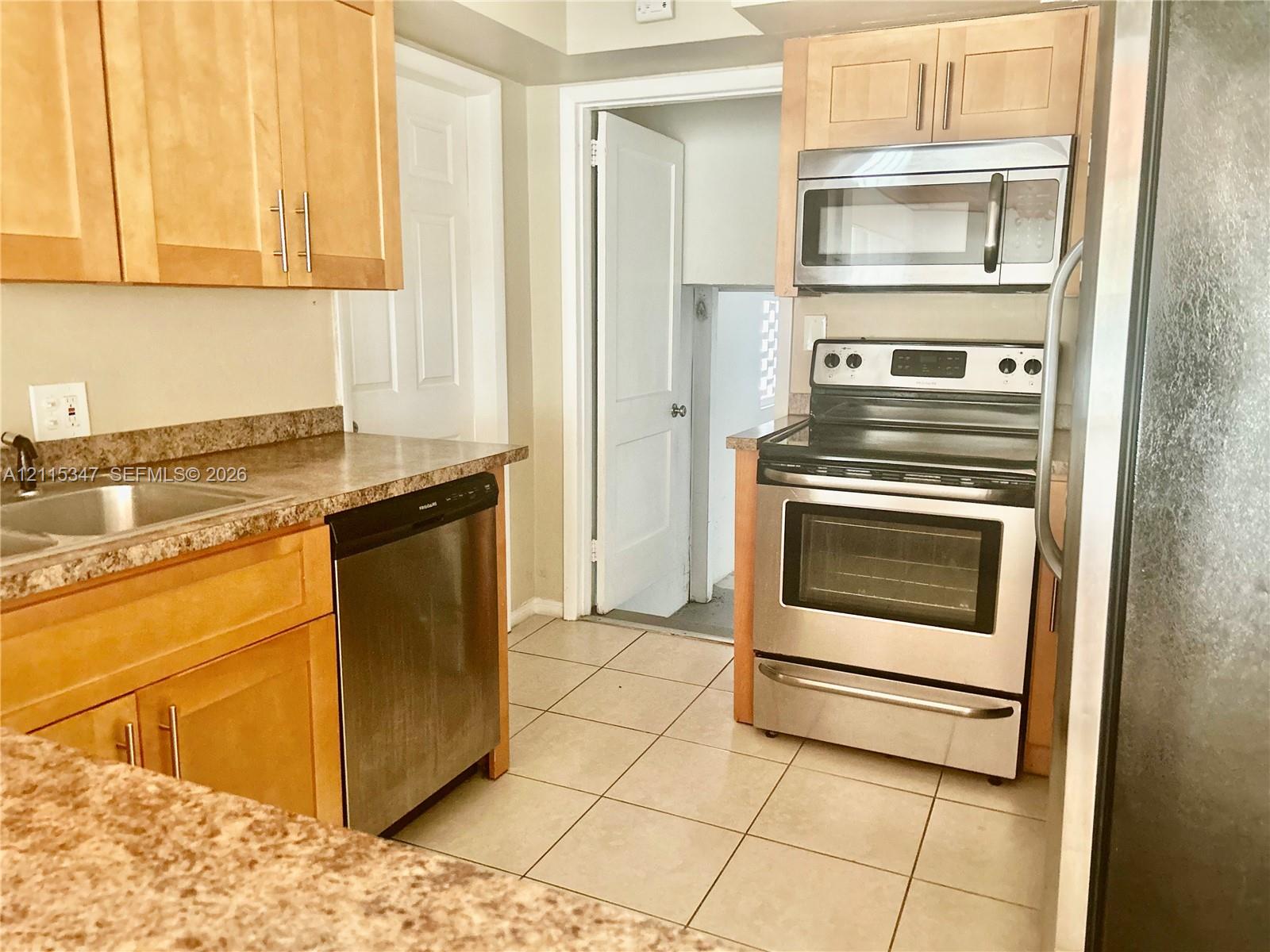 Kitchen featuring light wood cabinetry, stone-finish laminate countertops, tile flooring, and stainless steel appliances including a range, microwave, and dishwasher
