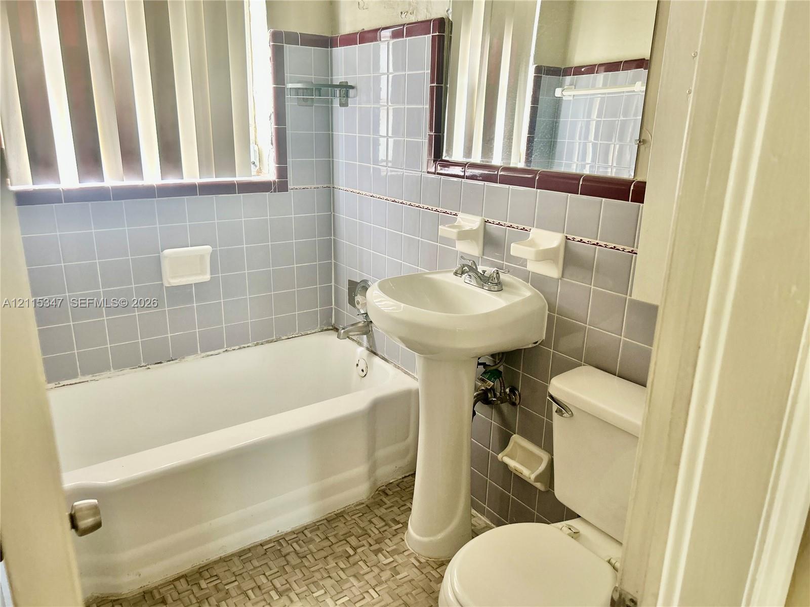 Full bathroom featuring a white pedestal sink, a porcelain bathtub, ceramic wall tiling with decorative trim, and patterned tile flooring