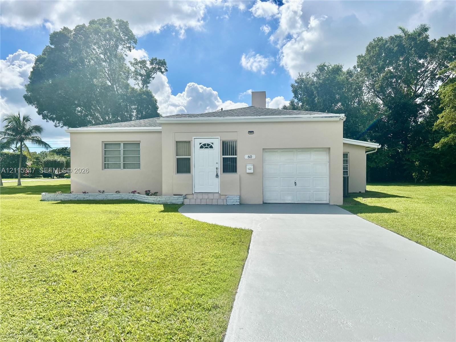 Single-story residence featuring a smooth stucco exterior, a concrete driveway, an attached single-car garage, a low-profile roof, and a prominent lawn