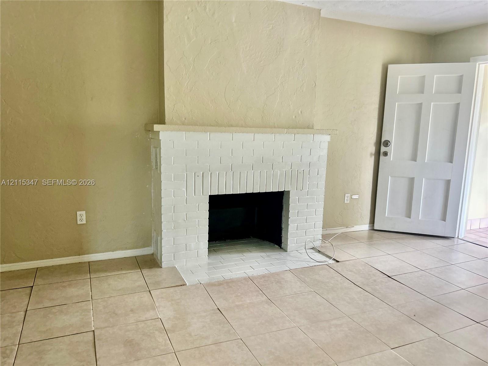 Fireplace featuring a painted brick surround and a stone mantel, complemented by large-format neutral floor tile and a six-panel door