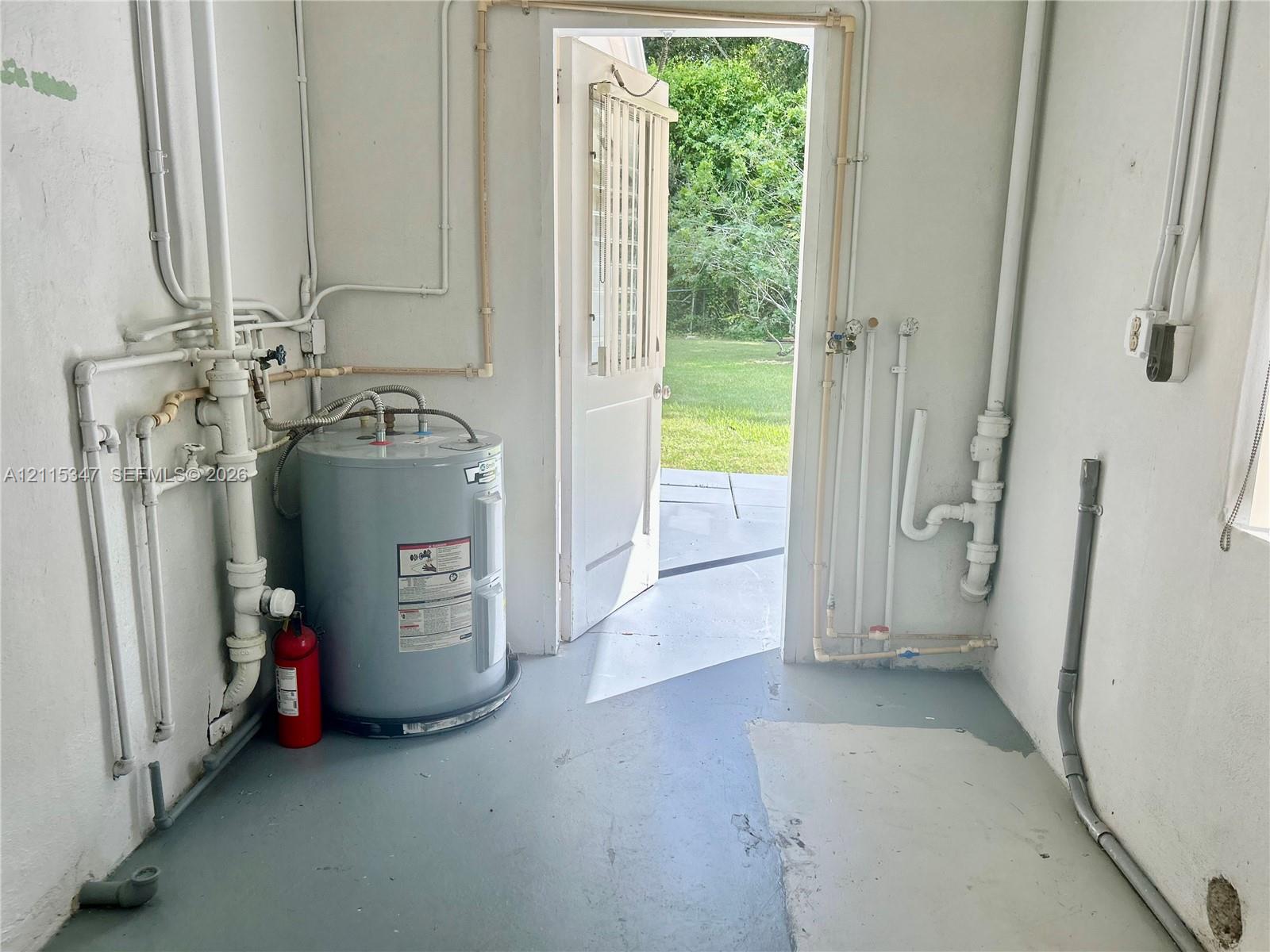 Utility space featuring an electric water heater, exposed plumbing lines, and a glass-panel exterior door leading to a grass-covered backyard