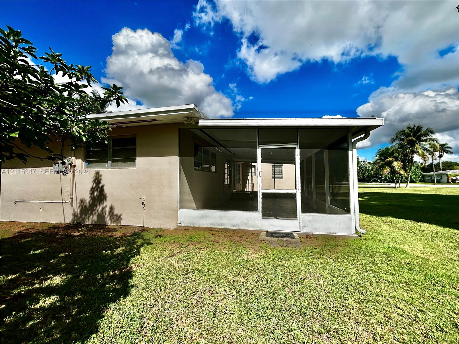 Stucco exterior featuring a screened-in lanai with aluminum framing and an expansive rear lawn
