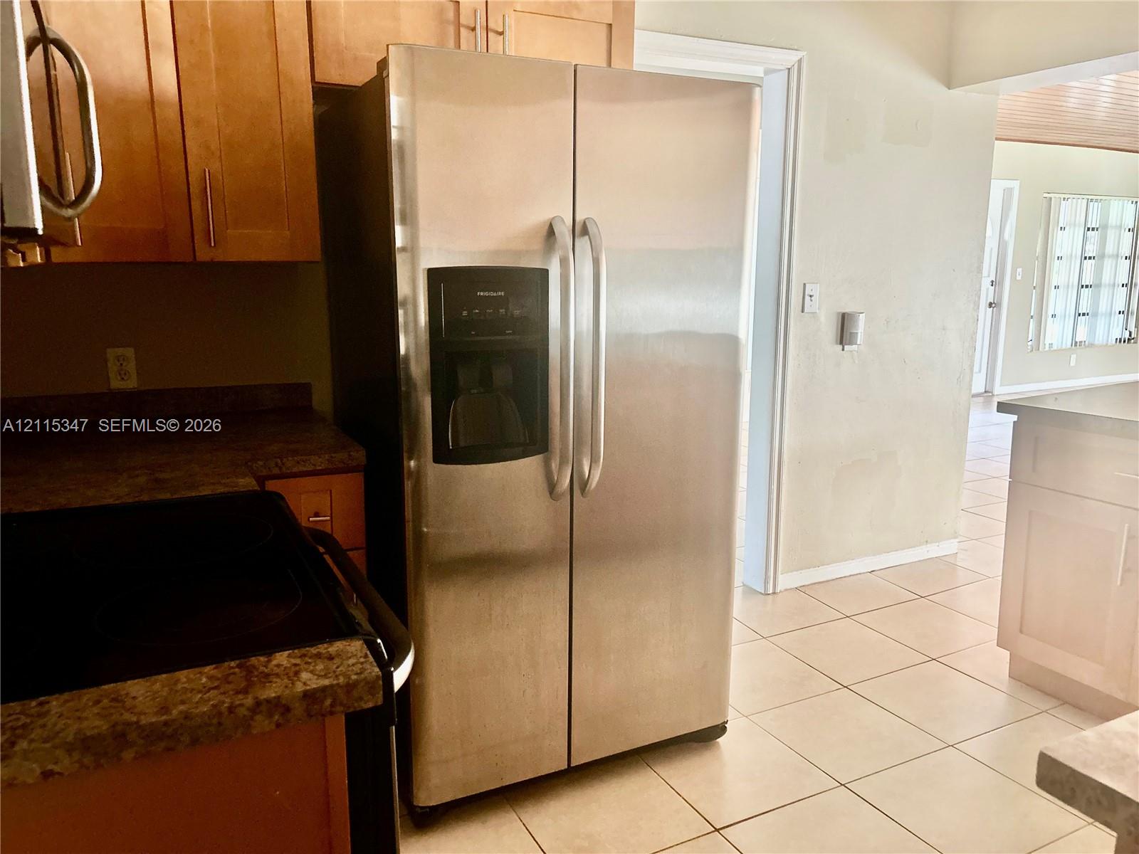 Stainless steel side-by-side refrigerator with integrated ice and water dispenser, light-finish cabinetry, stone-texture countertops, and tile flooring