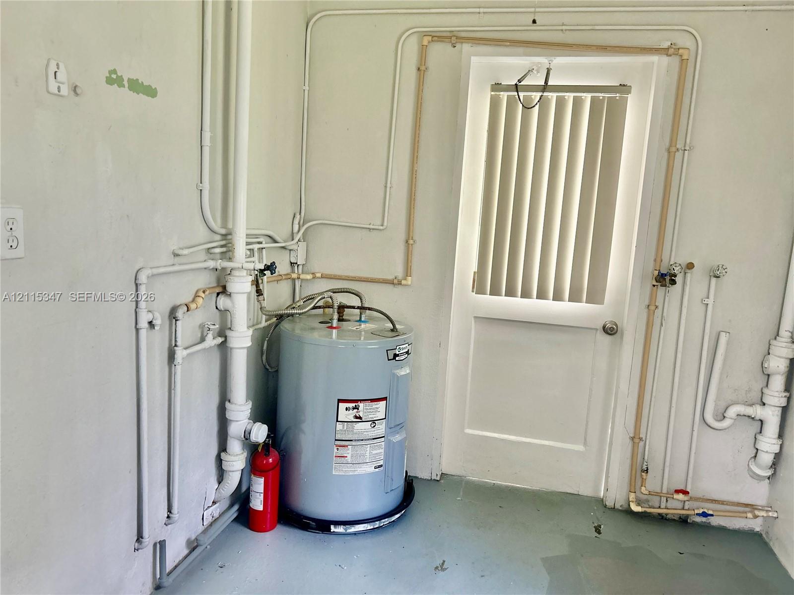 Utility area featuring a water heater, exposed plumbing lines, and an exterior door with vertical blinds