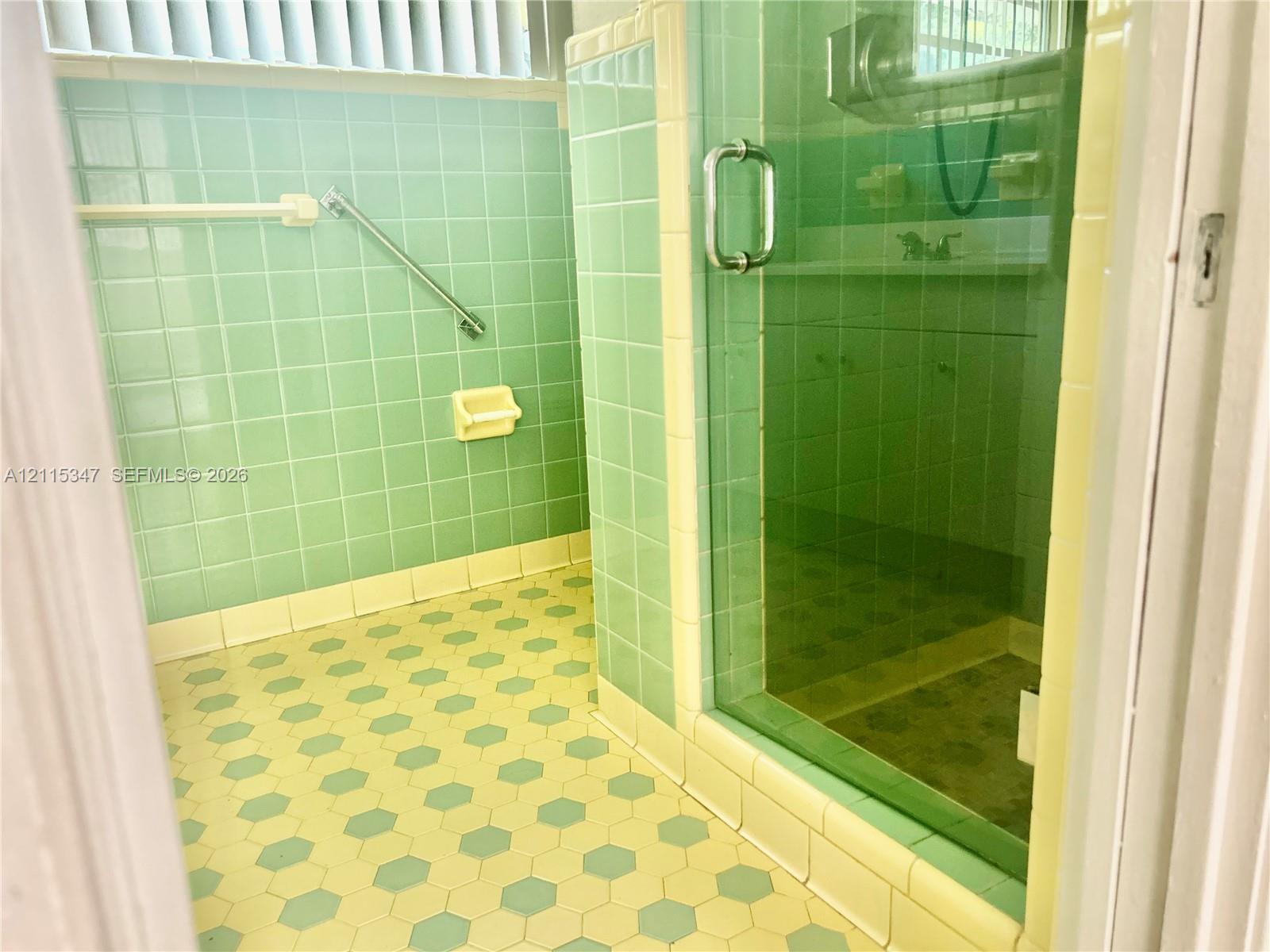 Bathroom featuring square ceramic wall tiles, hexagonal floor tiles, a glass-enclosed shower, and mounted metal hardware