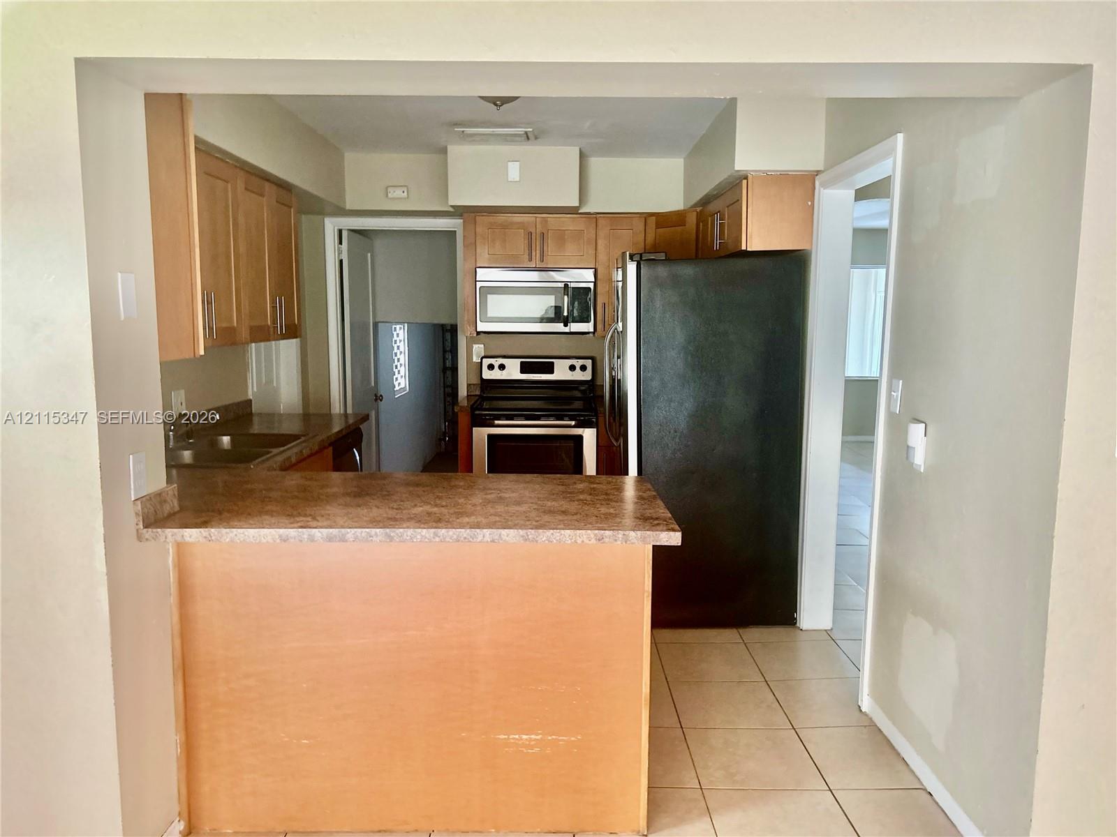 Kitchen featuring natural wood-finish cabinetry, laminate countertops, a built-in microwave, stainless steel range, and tile flooring