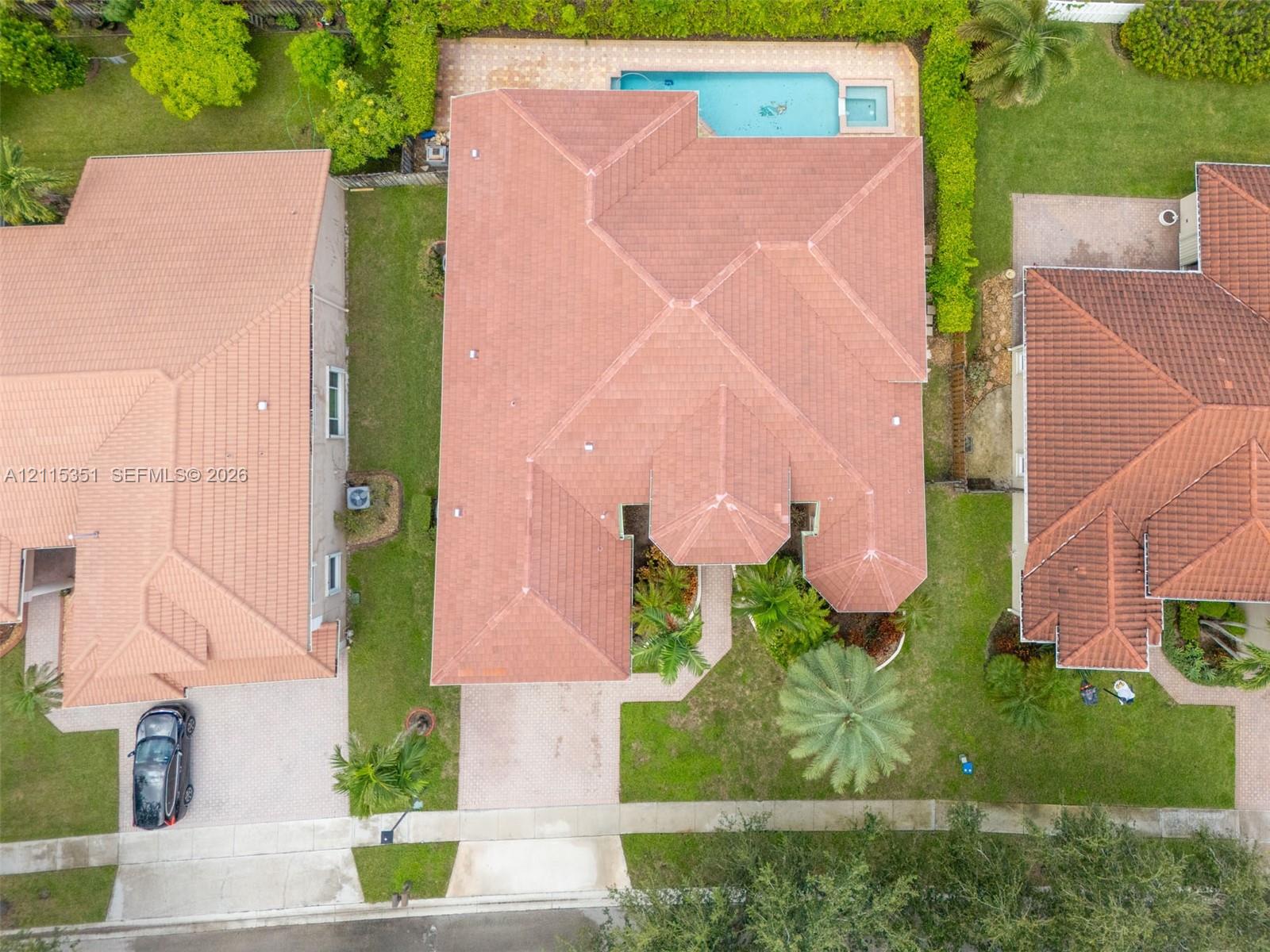Aerial perspective featuring a tile roof, paved driveway, swimming pool with attached spa, and mature landscaping