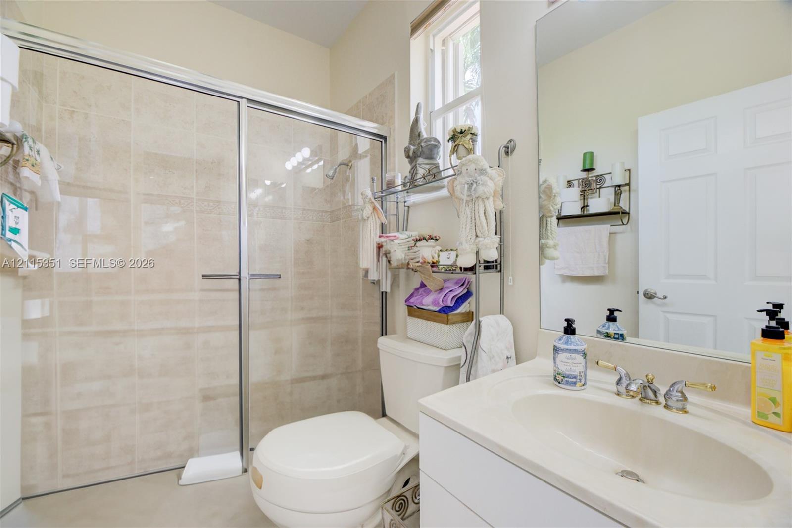 Bathroom featuring a shower stall with a glass enclosure, light-toned wall tile, a vanity with an integrated basin, a polished faucet, and a large wall-mounted mirror