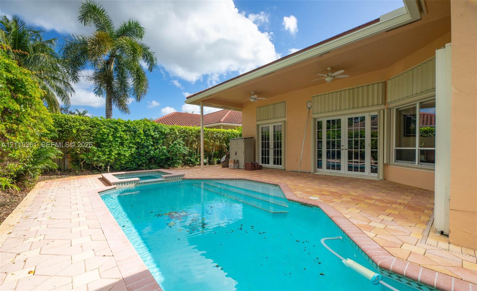 In-ground swimming pool with an integrated spa, paver patio, covered lanai, and glass-paned double doors