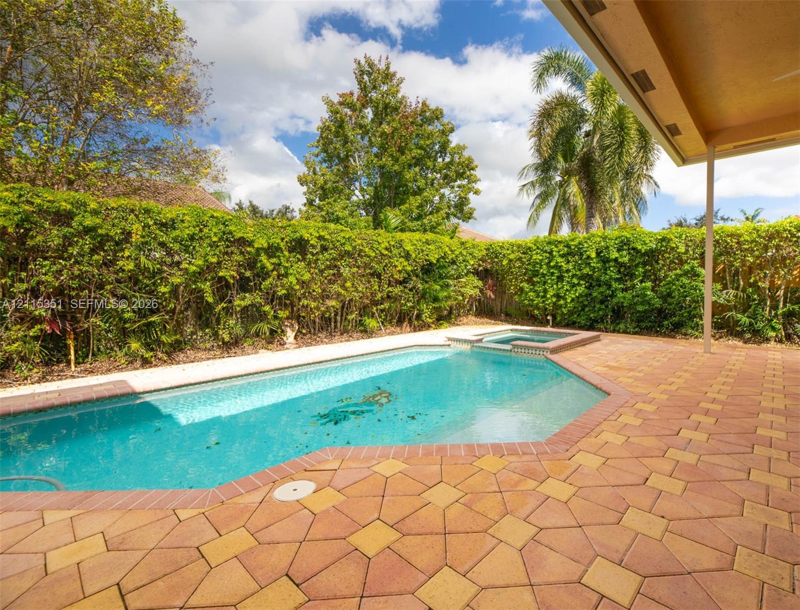 Swimming pool with integrated spa, paver patio, covered porch, and mature perimeter hedging
