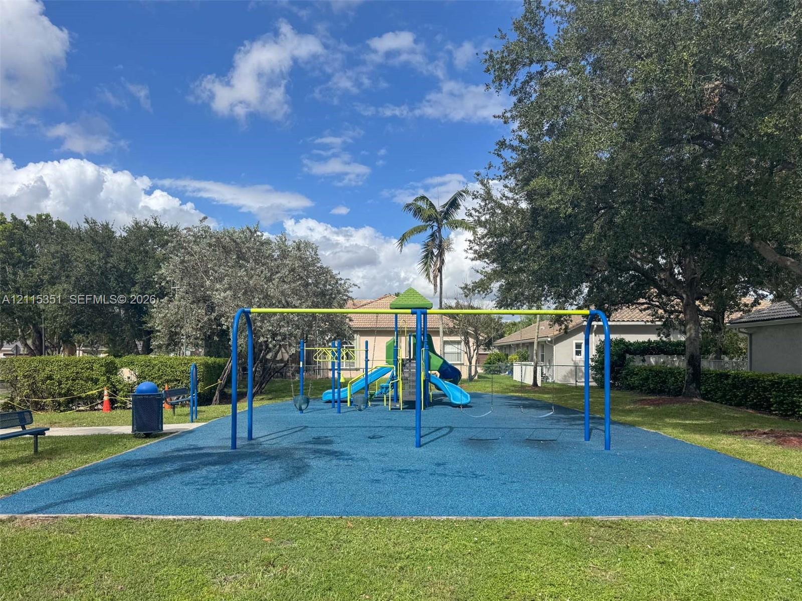 Community recreation area featuring a playground structure with slides, swing sets, a poured-in-place rubberized surface, and mature landscaping