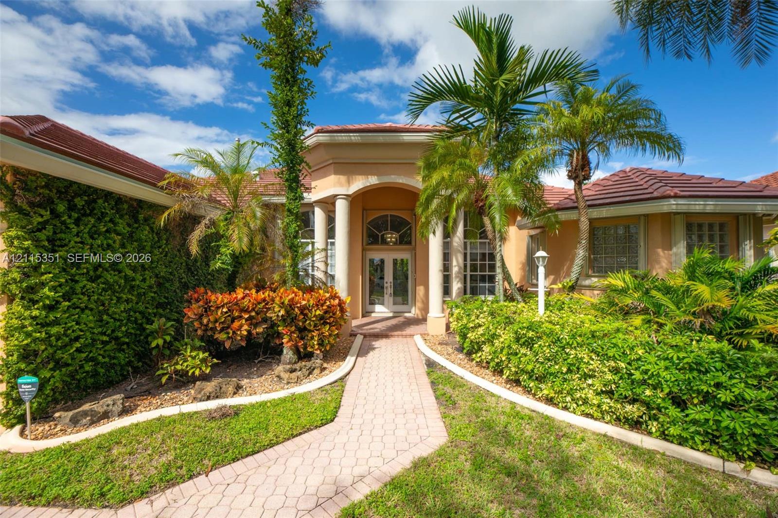 Stucco exterior featuring a tiled hip roof, arched entryway with dual columns, and a paver walkway leading to glass-paneled double doors