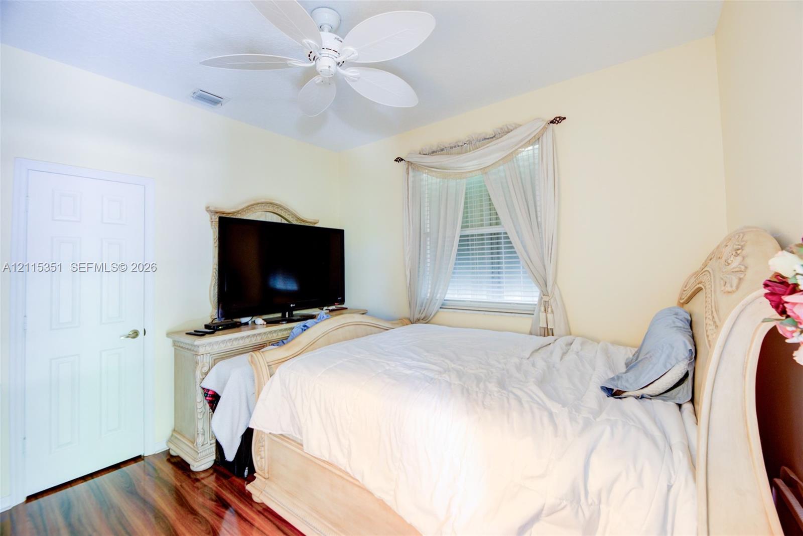 Polished wood-finish flooring, ceiling-mounted multi-blade fan, and window featuring horizontal blinds