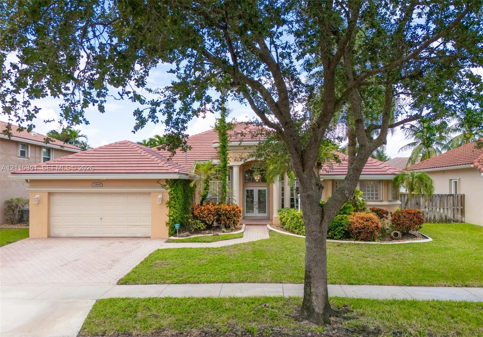 Single-story residence featuring a tiled roof, arched entryway with decorative columns, brick-paver driveway, and manicured landscaping