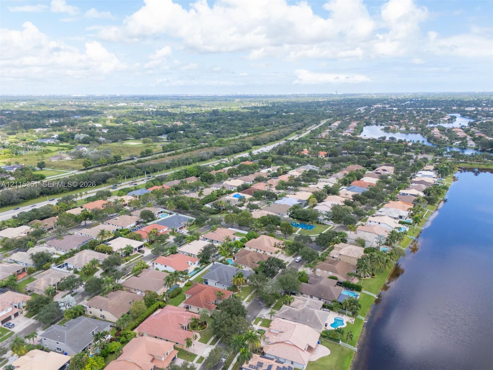 Aerial perspective of a residential community featuring extensive waterfront acreage, paved roadways, and dense mature landscaping