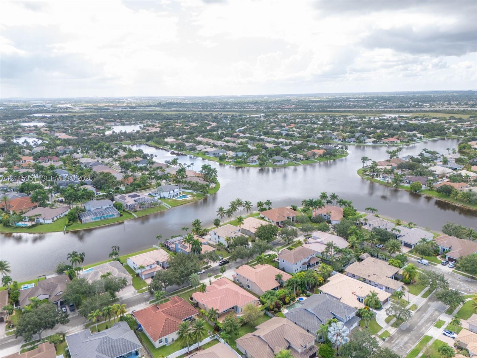 Aerial perspective of a waterfront residential community featuring expansive canal systems, tile-roofed housing, and established tropical landscaping