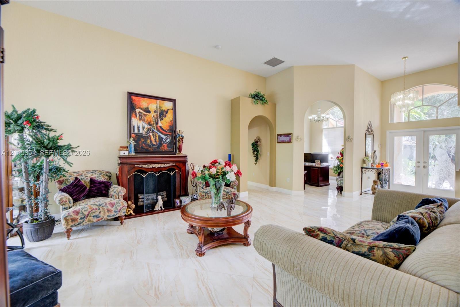 Living space featuring vaulted ceilings, polished tile flooring, a fireplace with a decorative mantel, arched entryways, and glass-paned double entry doors with an arched transom window Living space featuring vaulted ceilings, polished tile flooring, a fireplace with a decorative mantel, arched entryways, and glass-paned double entry doors with an arched transom window