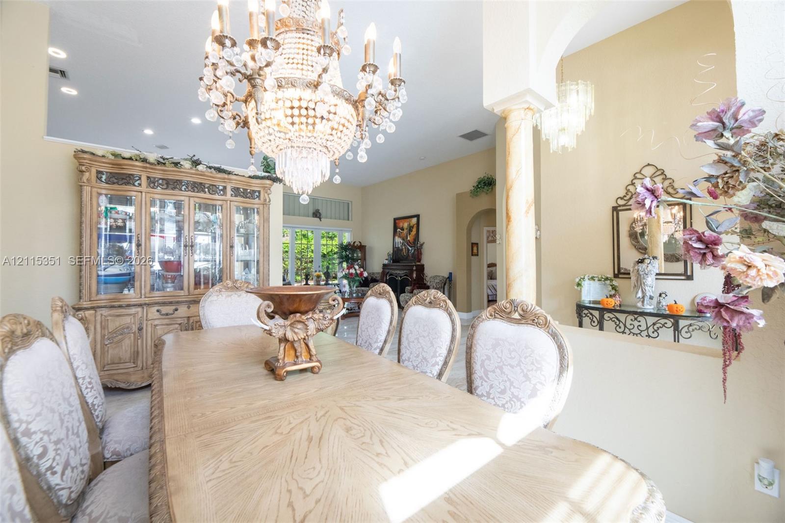 Dining area featuring high ceilings, a decorative crystal chandelier, a classic column, and arched entryways