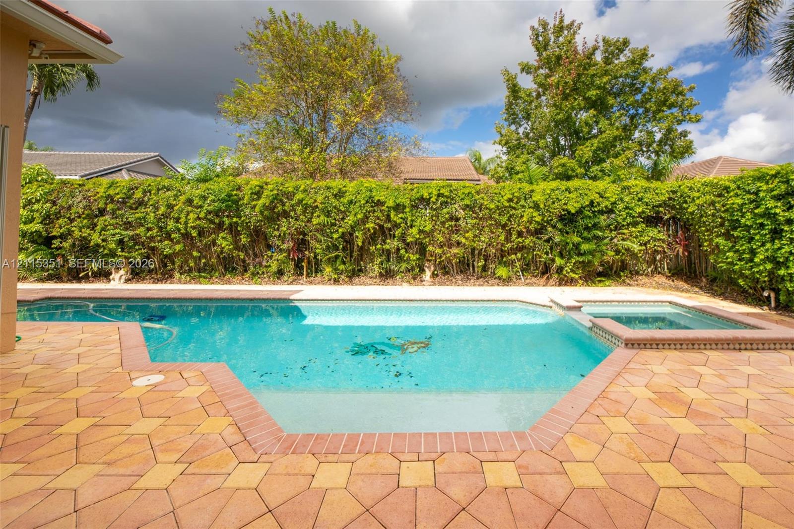 Outdoor pool with integrated spa, bordered by patterned paver decking and high-density privacy shrubbery