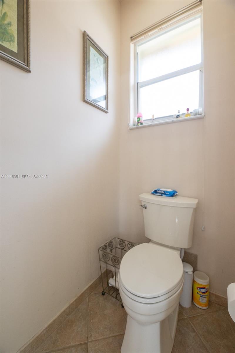 Standard-height toilet with a dual-flush tank and a multi-pane window with a neutral tile floor