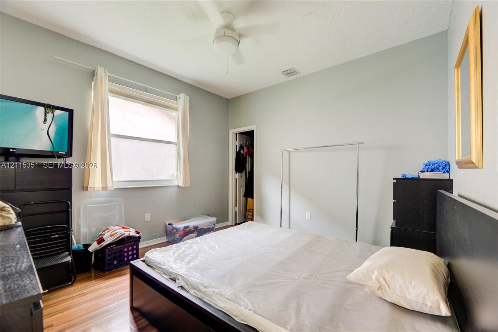 Room featuring wood-finish flooring, a ceiling fan with integrated lighting, and a window with horizontal blinds