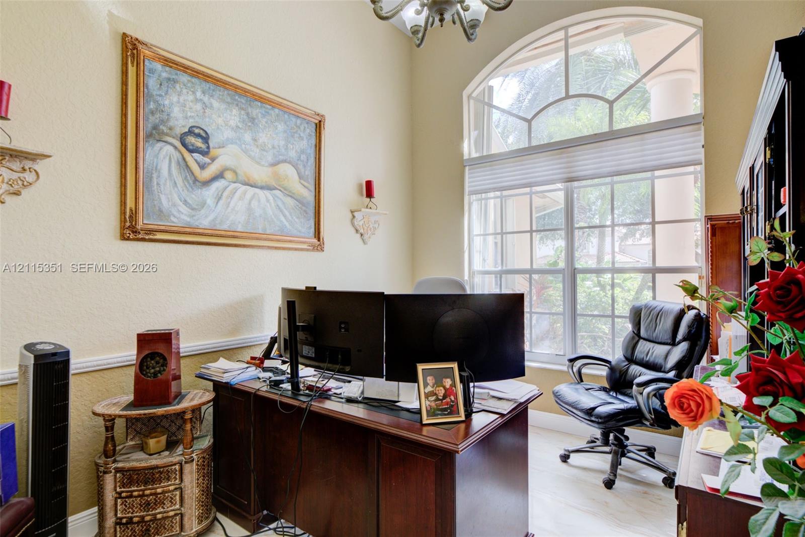 High-ceiling room featuring an arched transom window, light-toned tile flooring, chair rail molding, and a decorative chandelier