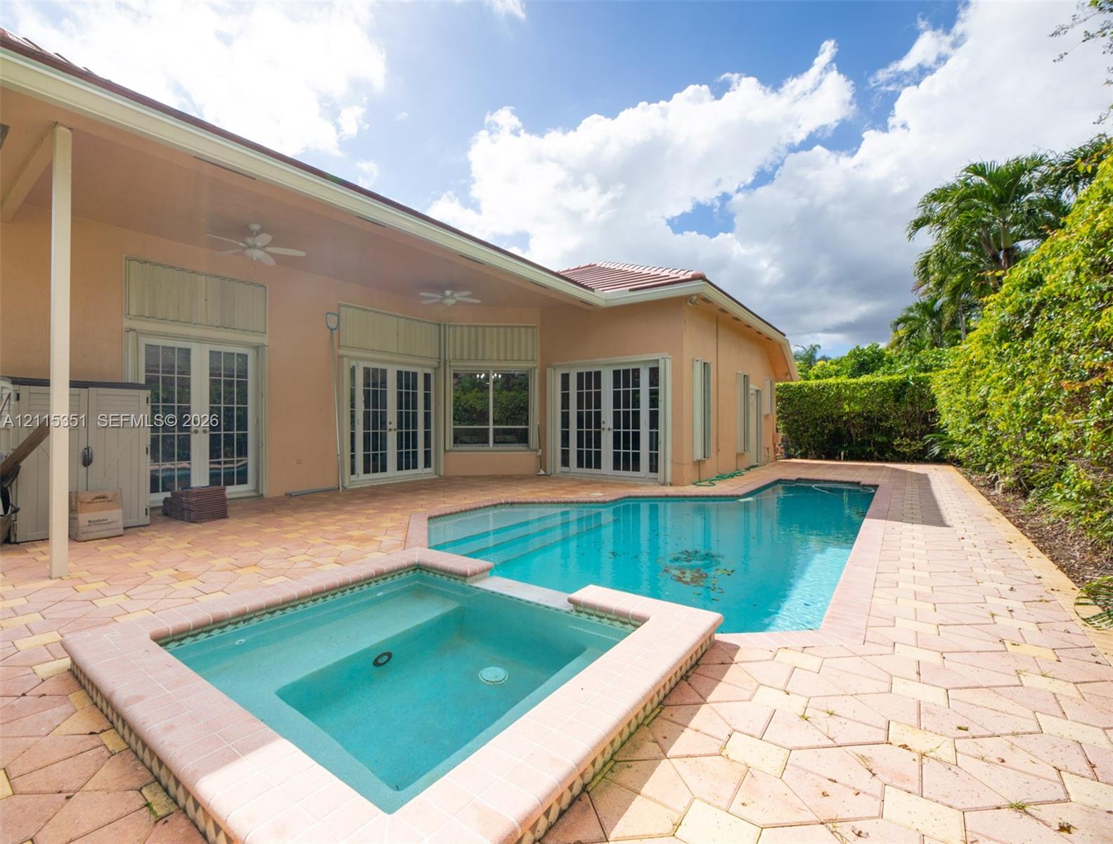 Covered patio with stone-paver decking, integrated swimming pool, attached spa, and multi-panel French doors
