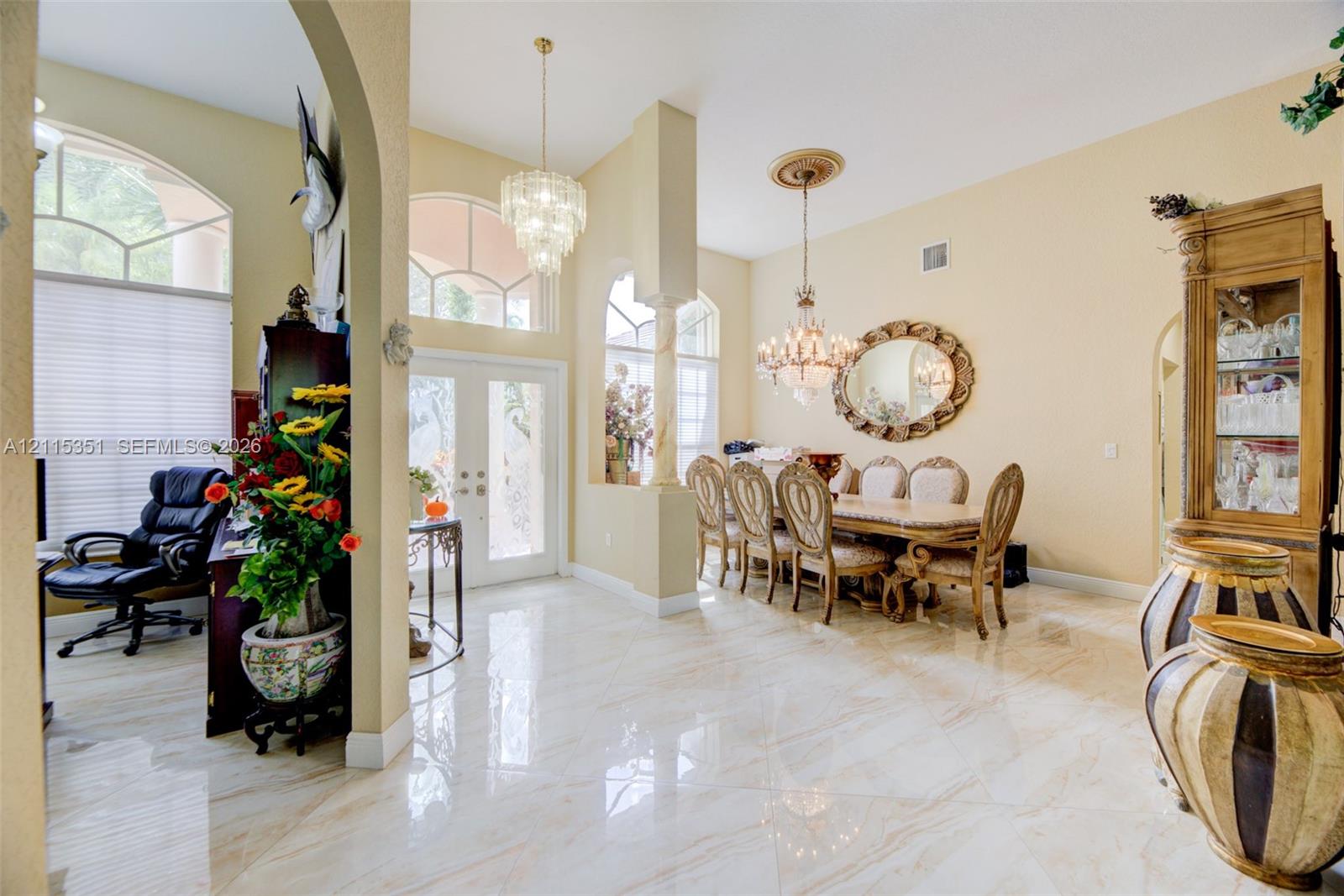 High-ceiling foyer featuring polished tile flooring, arched entryways, decorative columns, and dual crystal chandeliers High-ceiling foyer featuring polished tile flooring, arched entryways, decorative columns, and dual crystal chandeliers