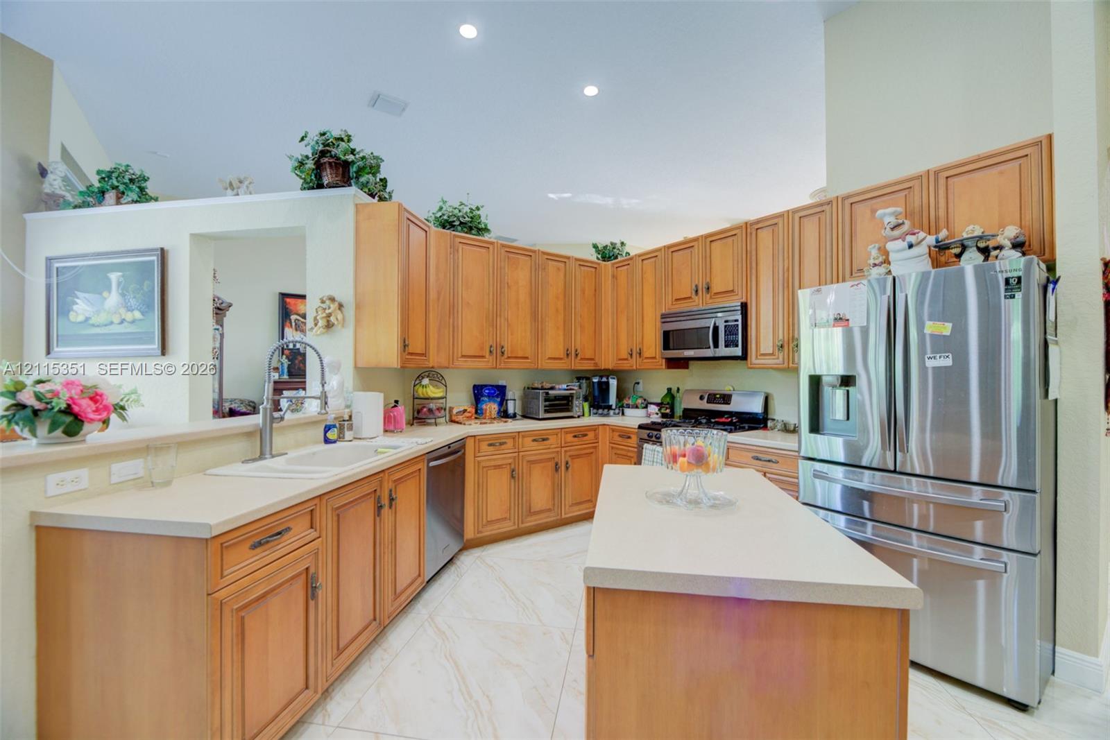 Kitchen featuring wood cabinetry, stone-finish countertops, stainless steel refrigerator, center island, and tile flooring