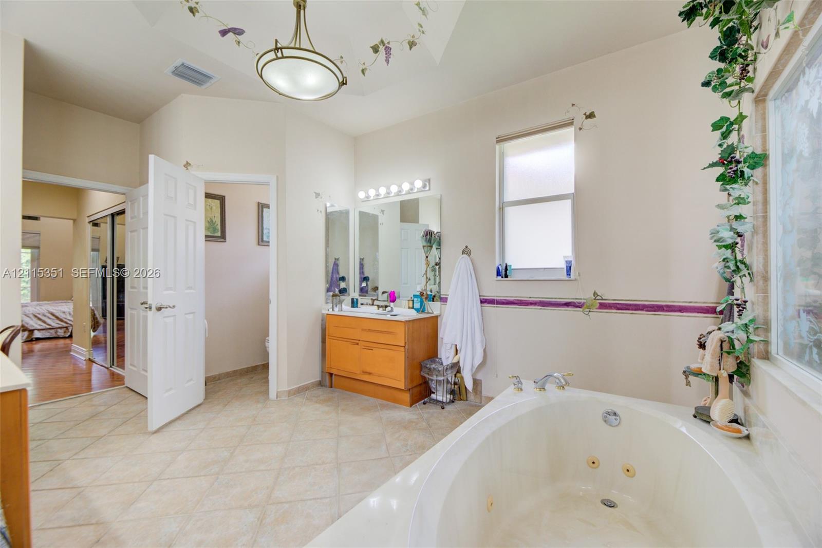 Bathroom featuring a jetted soaking tub, wood-finish vanity, tiled flooring, multi-light wall fixture, and vaulted ceiling with a decorative pendant light
